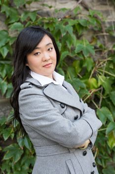 Young Asian woman standing next to leafs on a wall crossing her arms