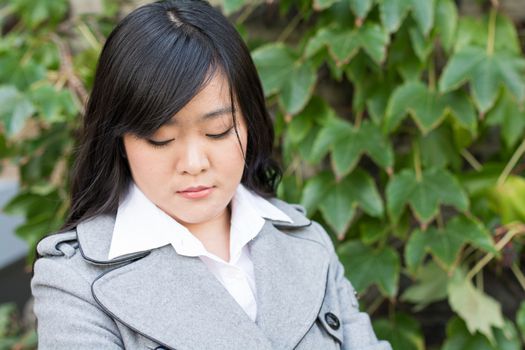 Young Asian woman standing next to leafs on a wall looking sad