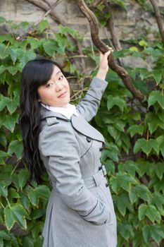 Young Asian woman standing next to leafs on a wall holding a branch