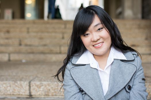 Young Asian woman in sitting on stairs in front of a business building