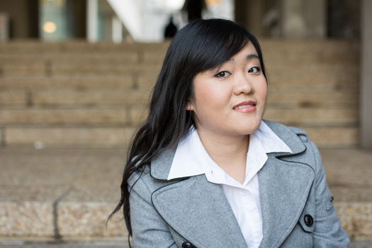 Young Asian woman in sitting on stairs in front of a business building