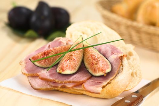 Fresh fig slices on smoked ham sandwich garnished with chives on sandwich paper with knife on the side (Selective Focus, Focus on the middle of the sandwich)