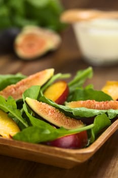 Fresh vegetarian salad made of fig, nectarine, spinach, cucumber and lettuce on wooden plate with jogurt sauce in the back (Selective Focus, Focus on the fig slice in the front)   