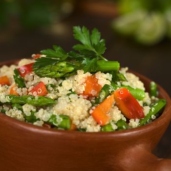 Vegetarian quinoa dish with green asparagus and red bell pepper, sprinkled with parsley in rustic bowl (Selective Focus, Focus on the asparagus heads on the dish)    