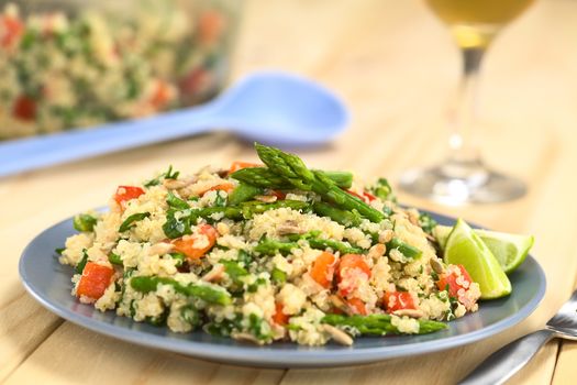 Vegetarian quinoa dish with green asparagus and red bell pepper, sprinkled with parsley and roasted sunflower seeds, lime wedges on the side (Selective Focus, Focus on the asparagus heads on the dish)    