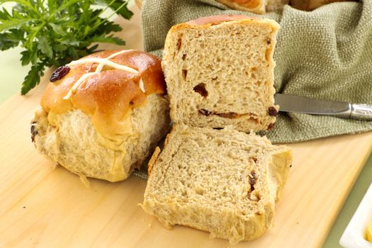 Hot cross buns with sliced open on a bread board.