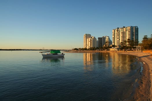 Boat sits in a quiet bay by the buildings on the shore at sunrise.