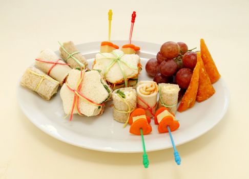 Healthy afternoon kids snack including sandwiches, carrots, cheese, grapes and an apricot wedge.