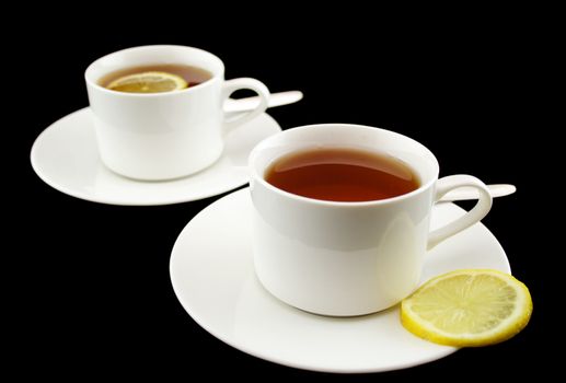 Two white cups of lemon tea over a black background.