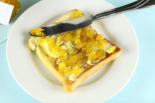 Orange marmalade spread on a slice of toast with butter.