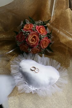Wedding rings on white pillow in the form of the heart near the wedding bouquet