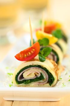 Crepe rolls as finger food filled with spinach and ham garnished with cherry tomato and watercress (Selective Focus, Focus on the right upper part of the crepe roll and the right part of the cherry tomato on top) 