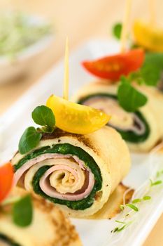 Crepe rolls as finger food filled with spinach and ham garnished with cherry tomato and watercress (Selective Focus, Focus on the right upper part of the crepe roll) 