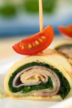 Crepe roll as finger food filled with spinach and ham garnished with cherry tomato (Selective Focus, Focus on the middle of the crepe roll and the lower edge of the cherry tomato on top) 