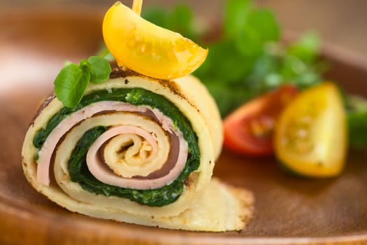 Crepe roll as finger food filled with spinach and ham garnished with cherry tomato and watercress served on wooden plate (Selective Focus, Focus on the upper part of the crepe roll) 