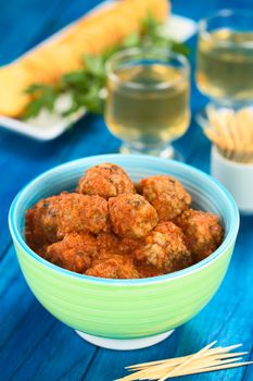Spanish albondigas (meatballs) in tomato sauce in colorful bowl with toothpick in the front, crackers and wine in the back on blue wood (Selective Focus, Focus on the meatballs on the top)