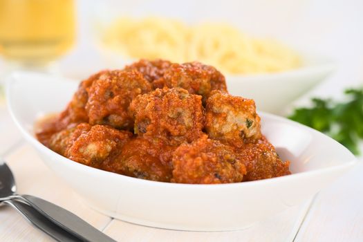 Spanish albondigas (meatballs) in tomato sauce in bowl with spaghetti and white wine in the back (Selective Focus, Focus on the meatballs on the top)