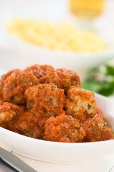 Spanish albondigas (meatballs) in tomato sauce in bowl with spaghetti and white wine in the back (Selective Focus, Focus on the meatballs on the top)