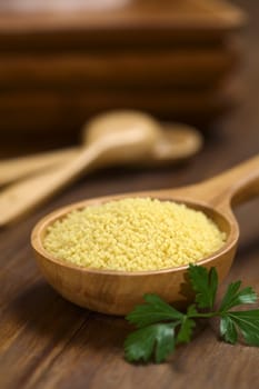 Raw couscous on wooden spoon with parsley leaf on the side (Very Shallow Depth of Field, Focus one third into the couscous)