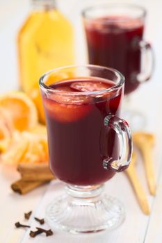 Hot spiced mulled red  wine with mandarin on top, with cloves, cinnamon sticks, mandarin, wooden spoon and a small bottle of rum (Selective Focus, Focus on the front of the rim and the handle of the glass) 