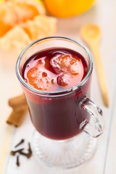 Hot spiced mulled red  wine with mandarin segments on top, with cloves, cinnamon sticks, mandarin and wooden spoon (Selective Focus, Focus one third into the mandarin segments on the drink) 