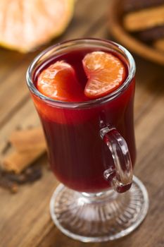 Hot spiced mulled red  wine with mandarin segments on top, with cloves and cinnamon on the side, cookies in the back (Selective Focus, Focus on the front of the right mandarin segment on the drink) 