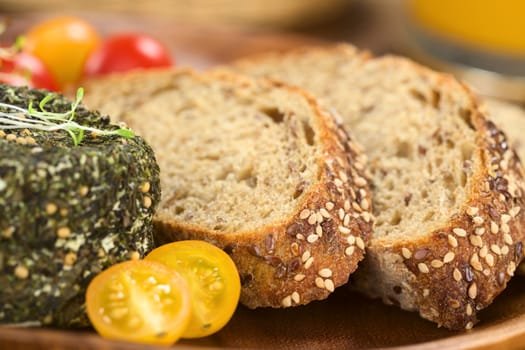 Slices of wholegrain bread with goat cheese covered with herbs and yellow cherry tomato (Selective Focus, Focus on the front of the bread slices)