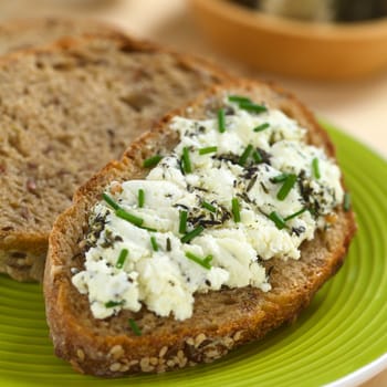 Slice of wholegrain bread spread with goat cheese with herbs with chives on top (Selective Focus, Focus one third into the cheese) 