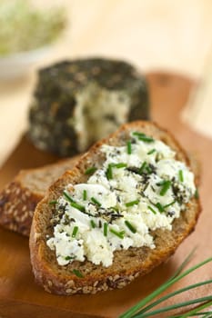 Slice of wholegrain bread spread with goat cheese with herbs with chives on top (Selective Focus, Focus one third into the cheese) 