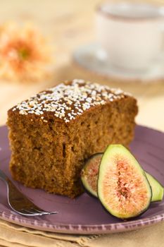 Fresh fig cake with fig halves on a purple plate with pastry fork (Selective Focus, Focus on the front upper corner of the cake and the middle of the fig half)