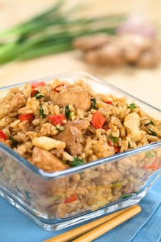 Homemade Chinese fried rice with vegetables, chicken and fried eggs served in glass bowl with chopsticks on the side (Selective Focus, Focus on the top of the dish)