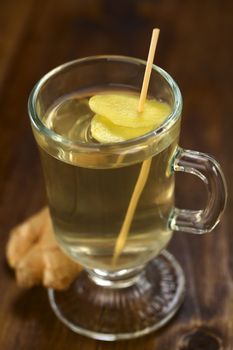 Freshly prepared hot ginger tea made of fresh ginger root, with ginger slices on skewer in the tea, served in glass (Selective Focus, Focus on the front of the upper ginger slice in the tea)