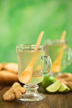 Freshly prepared hot ginger tea made of fresh ginger root served in glass (Selective Focus, Focus on the front of the rim and the handle of the glass and on the front of the ginger root next to it)