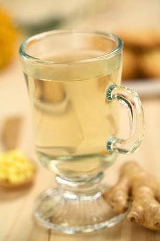 Freshly prepared hot ginger tea made of fresh ginger root served in glass (Selective Focus, Focus on the front of the rim and the handle of the glass)