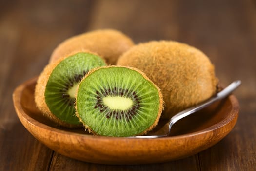 Kiwifruits on wooden plate with spoon (Selective Focus, Focus on the half kiwi)