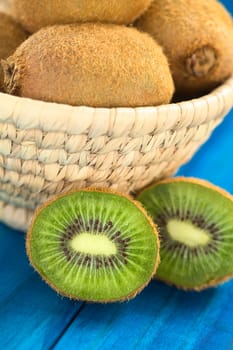 Half kiwi fruits on blue wood with kiwi fruits in basket behind (Selective Focus, Focus on the first half kiwi)