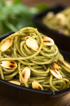 Pasta with pesto made of basil and spinach garnished with roasted almonds served in black bowl (Selective Focus, Focus on the almond half on the top of the dish)  