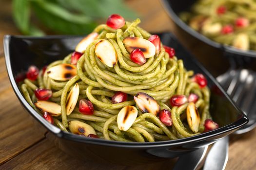 Pasta with pesto made of basil and spinach garnished with roasted almonds and pomegranate served in black bowl (Selective Focus, Focus on the almond and pomegranate just below the top of the dish)  
