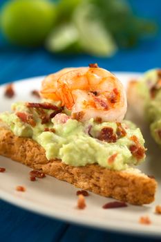 Wholegrain toast bread slice with guacamole, fried shrimp and fried bacon pieces (Selective Focus, Focus on the tail of the shrimp on the bread) 