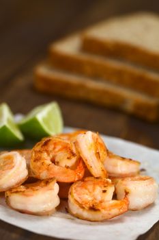 Fresh fried shrimps with lime wedges on sandwich paper with toast bread slices in the back (Selective Focus, Focus one third into the shrimps)