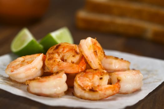 Fresh fried shrimps with lime wedges on sandwich paper with toast bread slices in the back (Selective Focus, Focus one third into the shrimps)