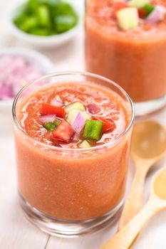 Traditional Spanish cold vegetable soup made of tomato, cucumber, bell pepper, onion, garlic and olive oil served in glasses (Selective Focus, Focus on the front of the vegetables on the top of the soup)