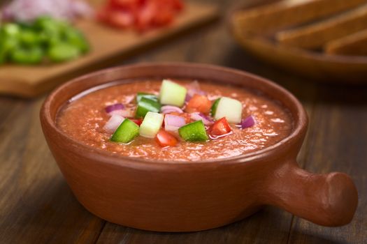 Traditional Spanish cold vegetable soup made of tomato, cucumber, bell pepper, onion, garlic and olive oil served in rustic bowl (Selective Focus, Focus on the front of the vegetables on the top of the soup)