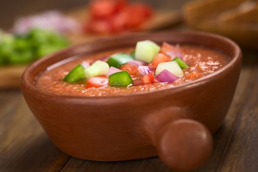 Traditional Spanish cold vegetable soup made of tomato, cucumber, bell pepper, onion, garlic and olive oil served in rustic bowl (Selective Focus, Focus on the front of the vegetables on the top of the soup)