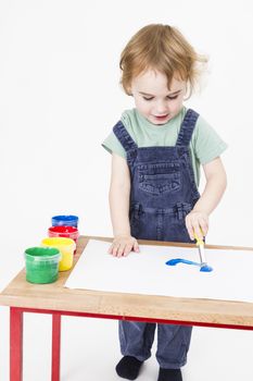 young girl working with paint on wooden desk. Studio shot in light grey background