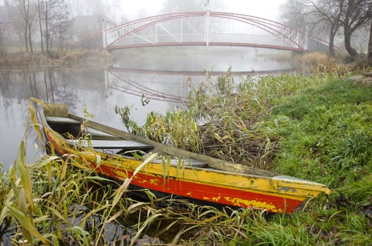 colorful old boat and river with bridge in autumn time morning mist