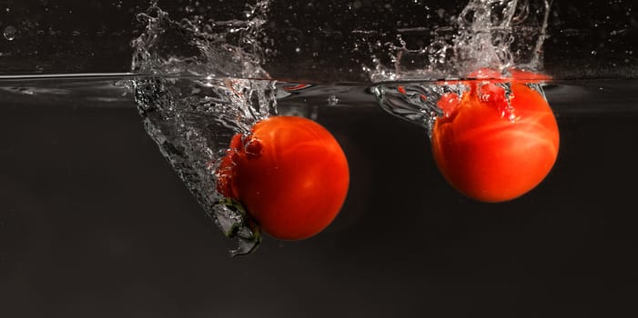 Fresh tomato dropped into water, isolated on dark background 