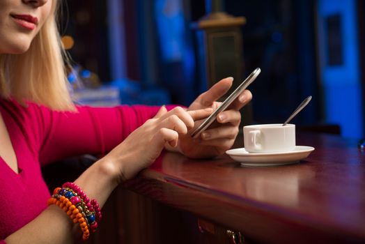 close-up of female hands holding a cell phone, sitting at the bar, next to a cup of coffee