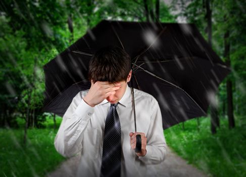 Sad Young Man walking with Umbrella under the Rain in the Summer Park