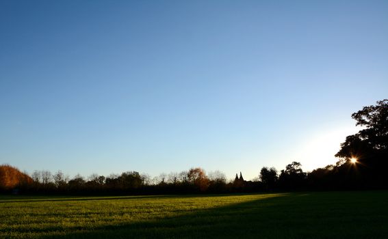 Silhouetted hedgerow and trees with oast houses backlit by sun setting beyond